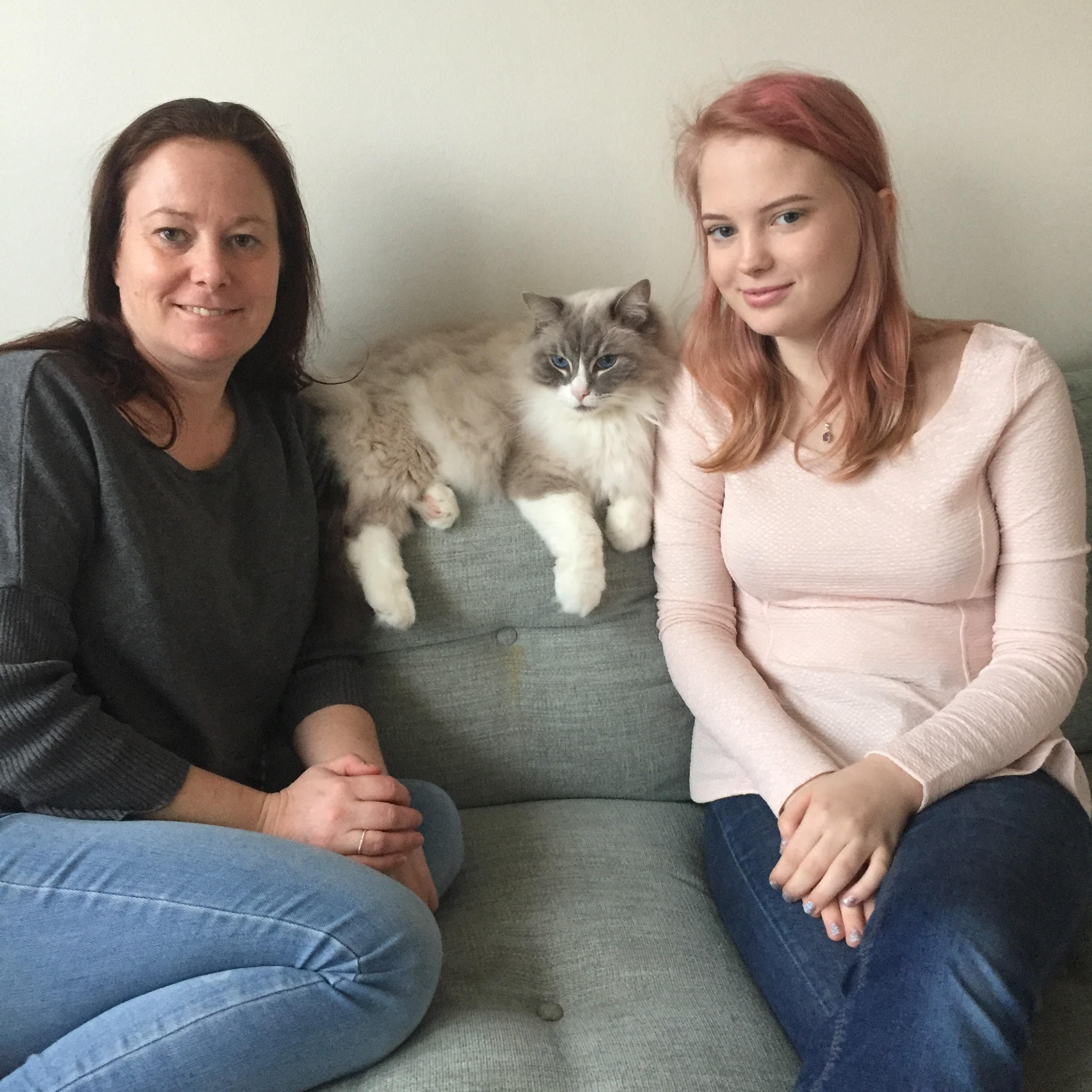 Vuxen kvinna och tonårsflicka sitter i en soffa, en katt ligger emellan dem