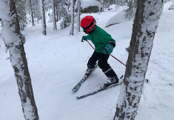 Pojke i grön jacka och röd hjälm som åker skidor